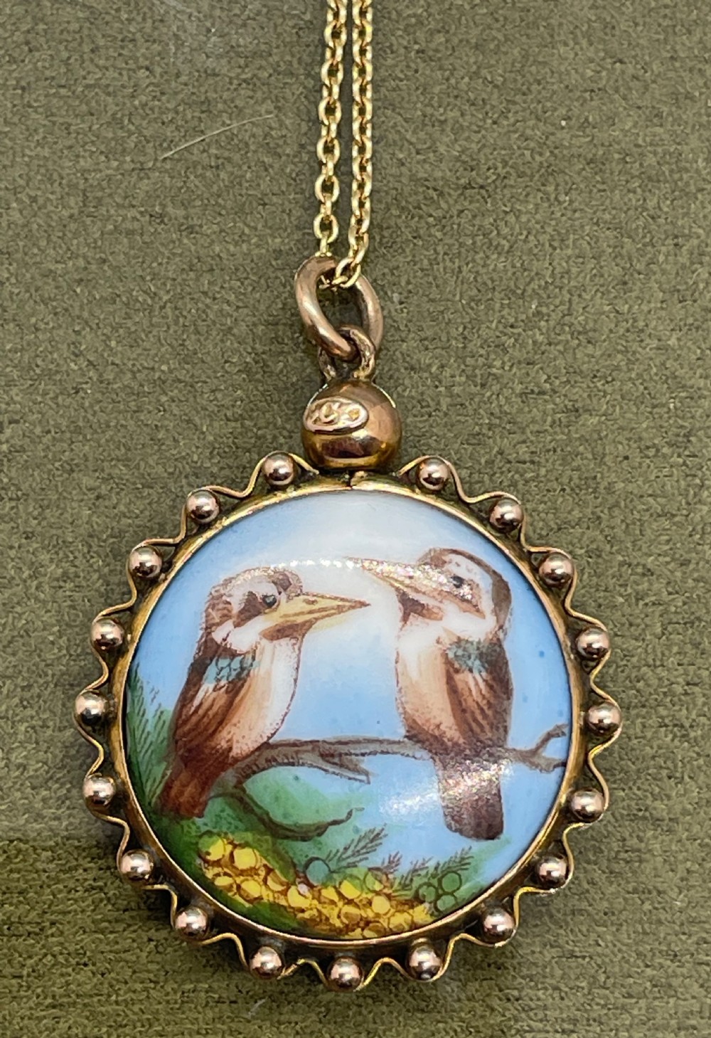 A circular late 19th-century 9ct gold pendant featuring a hand-painted enamel depiction of two kookaburras perched on a branch within a beaded border.