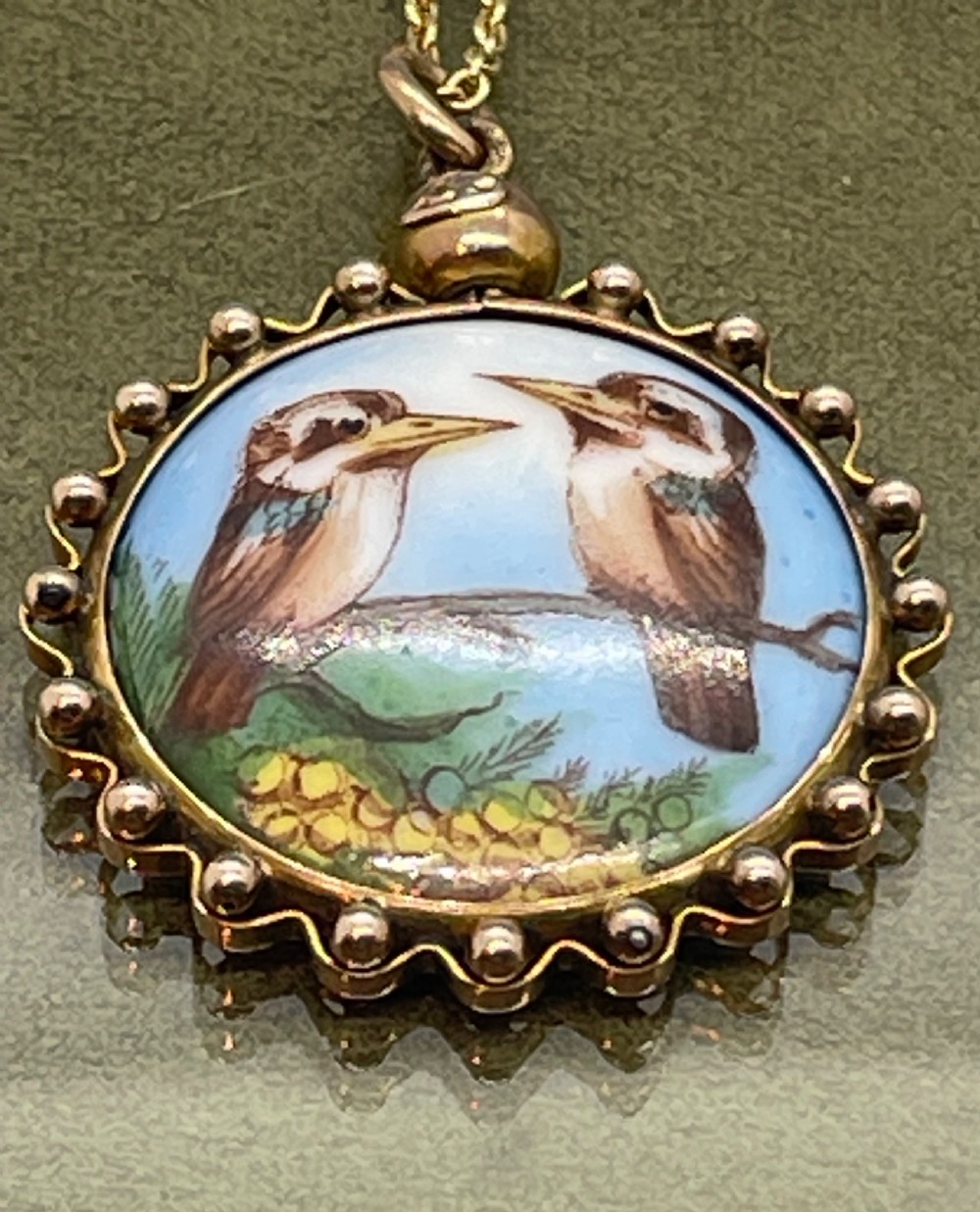 A circular late 19th-century 9ct gold pendant featuring a hand-painted enamel depiction of two kookaburras perched on a branch within a beaded border. View V