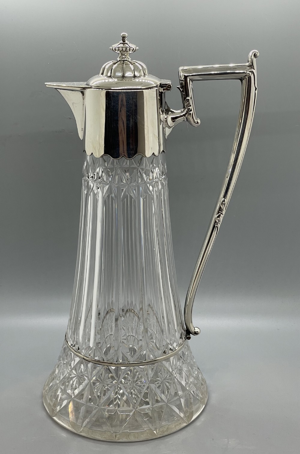A late Victorian cut-crystal claret jug featuring a fluted glass body, hallmarked sterling silver mounts, a hinged lid, and an angular handle.