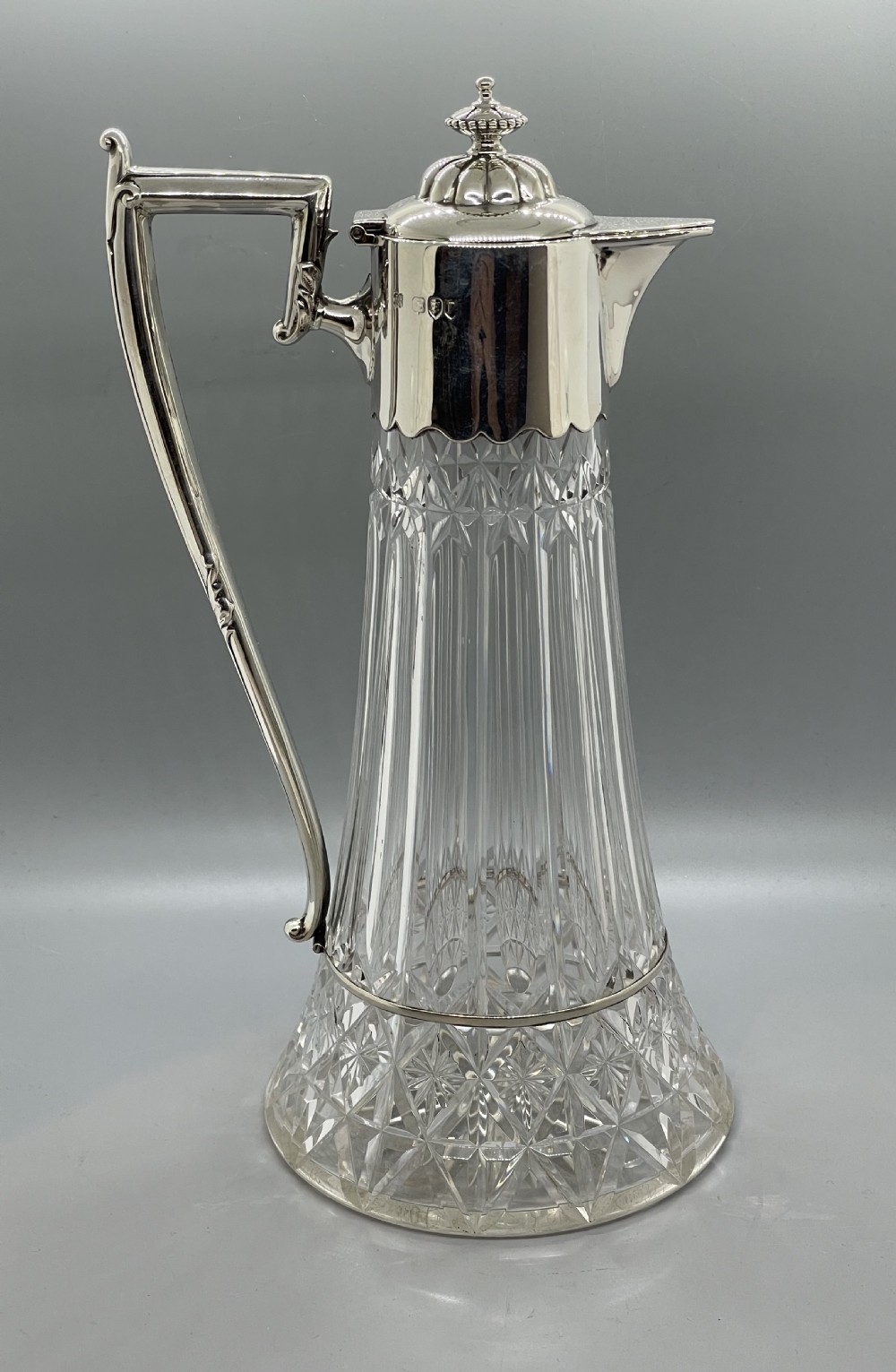 A late Victorian cut-crystal claret jug featuring a fluted glass body, hallmarked sterling silver mounts, a hinged lid, and an angular handle. View III