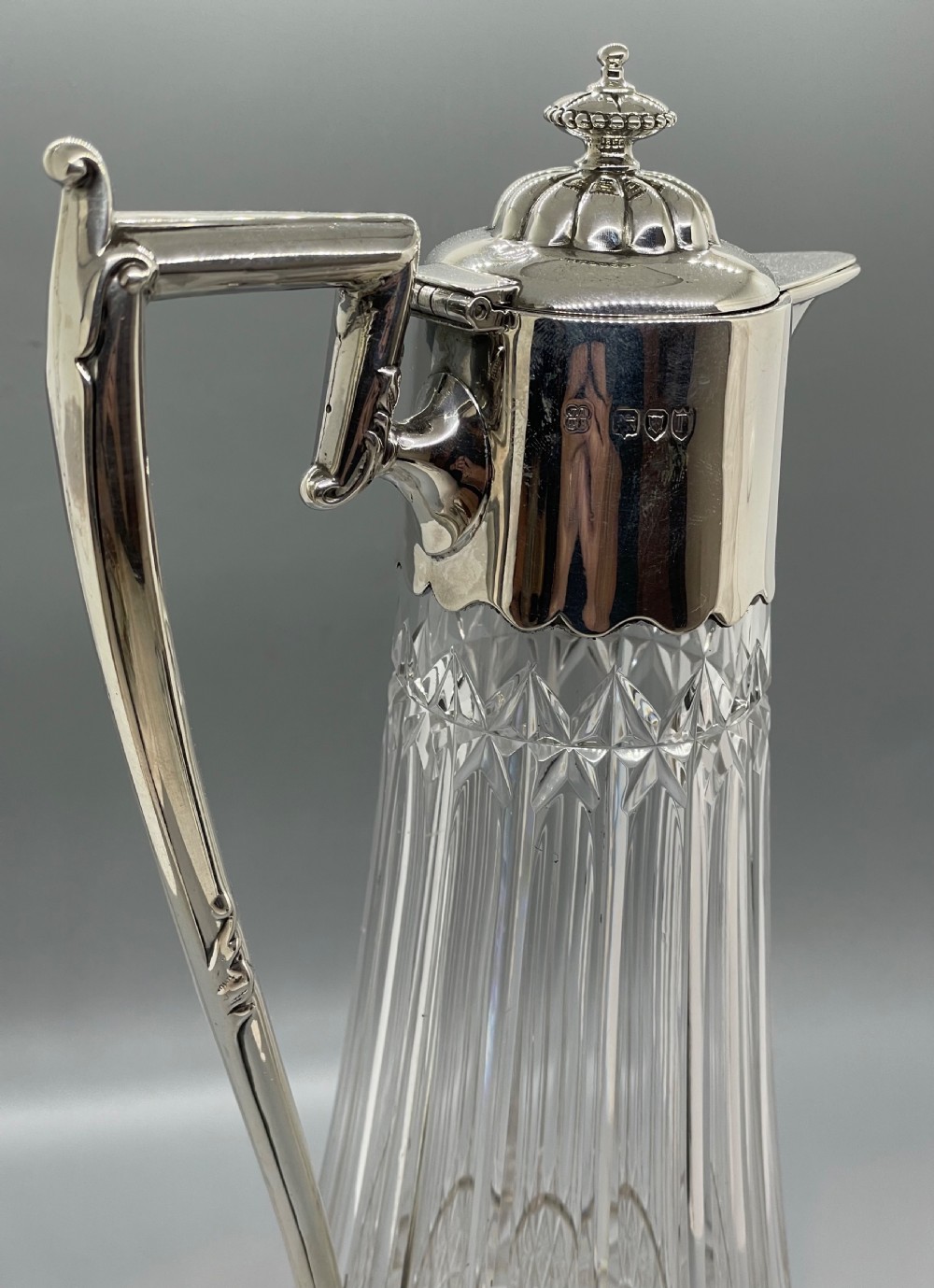 A late Victorian cut-crystal claret jug featuring a fluted glass body, hallmarked sterling silver mounts, a hinged lid, and an angular handle. View VII