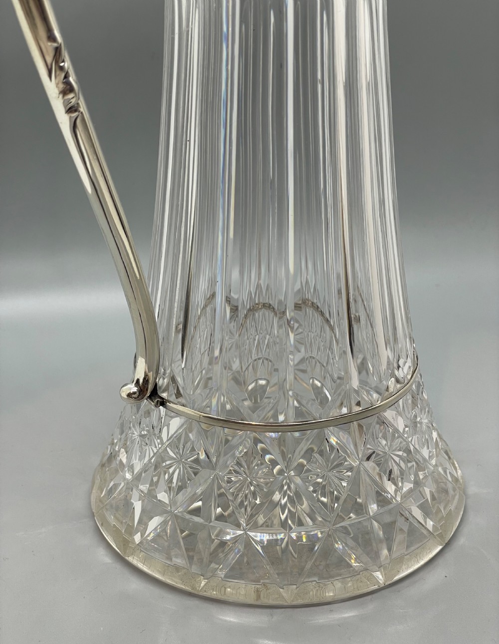 A late Victorian cut-crystal claret jug featuring a fluted glass body, hallmarked sterling silver mounts, a hinged lid, and an angular handle. View VIII