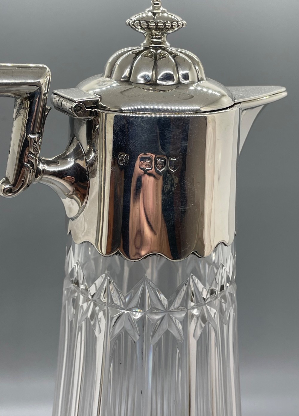 A late Victorian cut-crystal claret jug featuring a fluted glass body, hallmarked sterling silver mounts, a hinged lid, and an angular handle. View IX