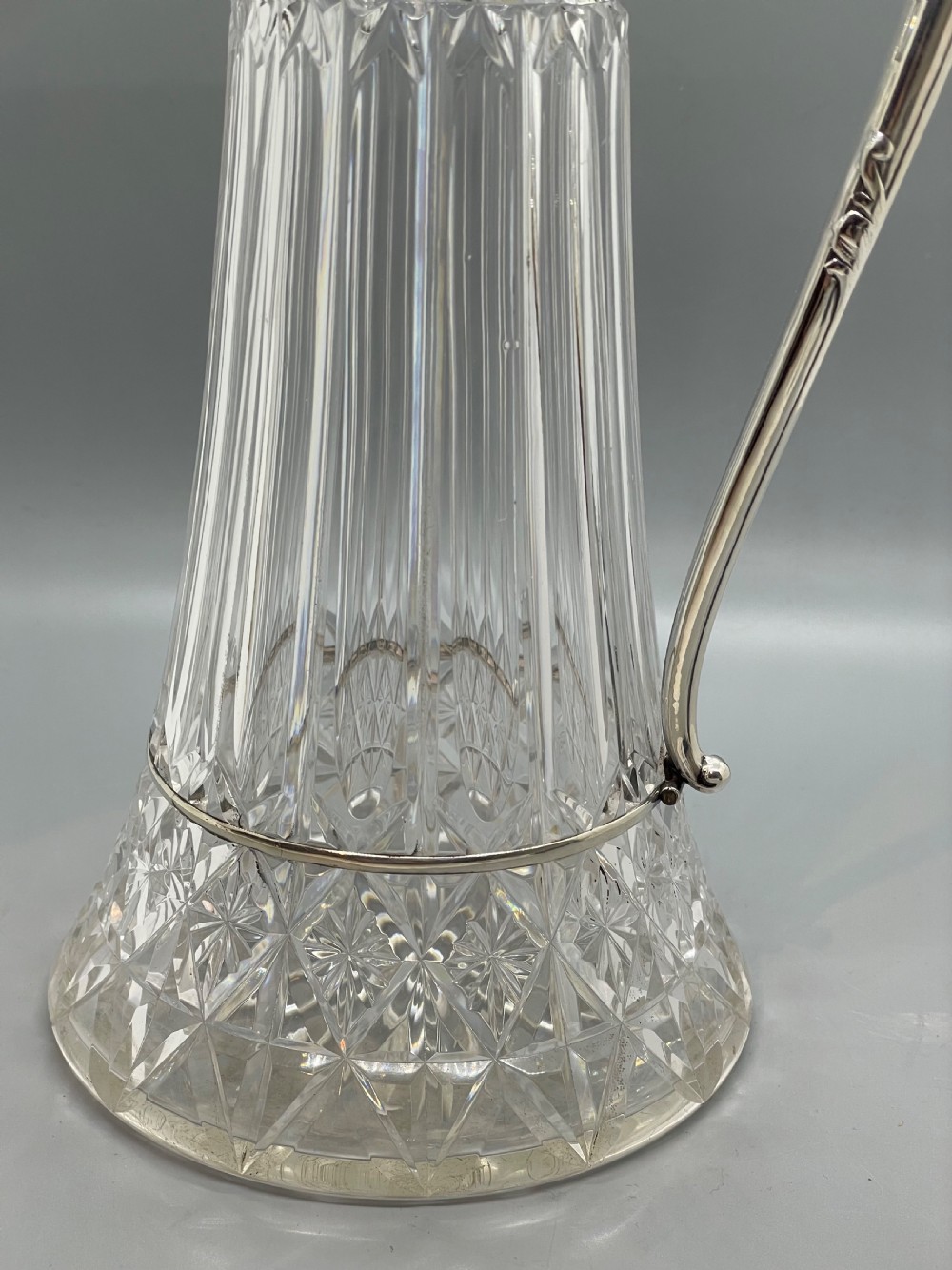 A late Victorian cut-crystal claret jug featuring a fluted glass body, hallmarked sterling silver mounts, a hinged lid, and an angular handle. View XI
