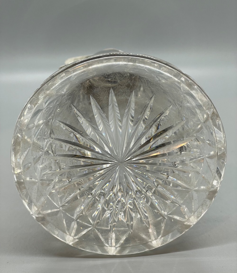 A late Victorian cut-crystal claret jug featuring a fluted glass body, hallmarked sterling silver mounts, a hinged lid, and an angular handle. View XII