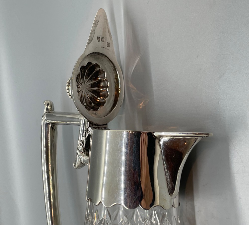 A late Victorian cut-crystal claret jug featuring a fluted glass body, hallmarked sterling silver mounts, a hinged lid, and an angular handle. View XIV