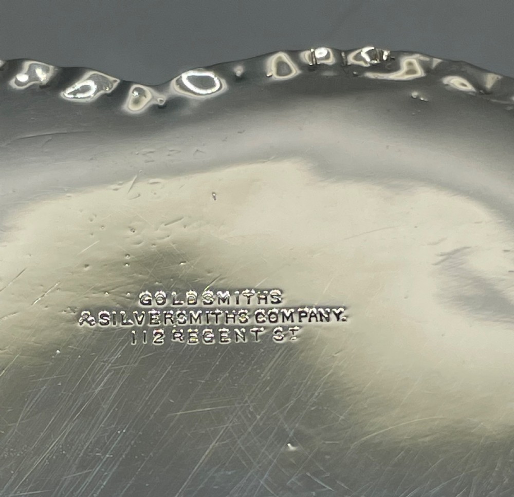 A heart-shaped sterling silver trinket box decorated with relief foliate scrollwork, a crimped rim, and a smooth central cartouche. View V