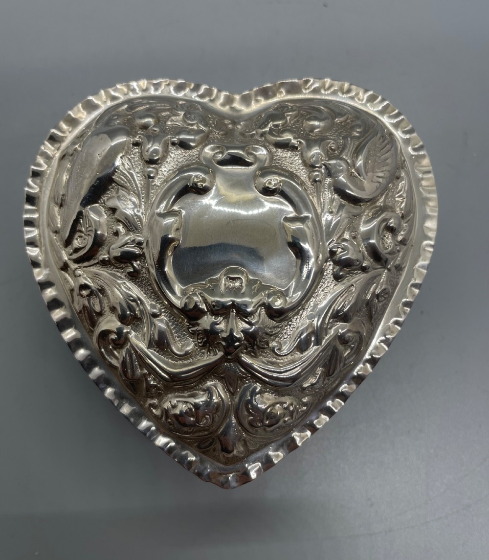A heart-shaped sterling silver trinket box decorated with relief foliate scrollwork, a crimped rim, and a smooth central cartouche. View VI
