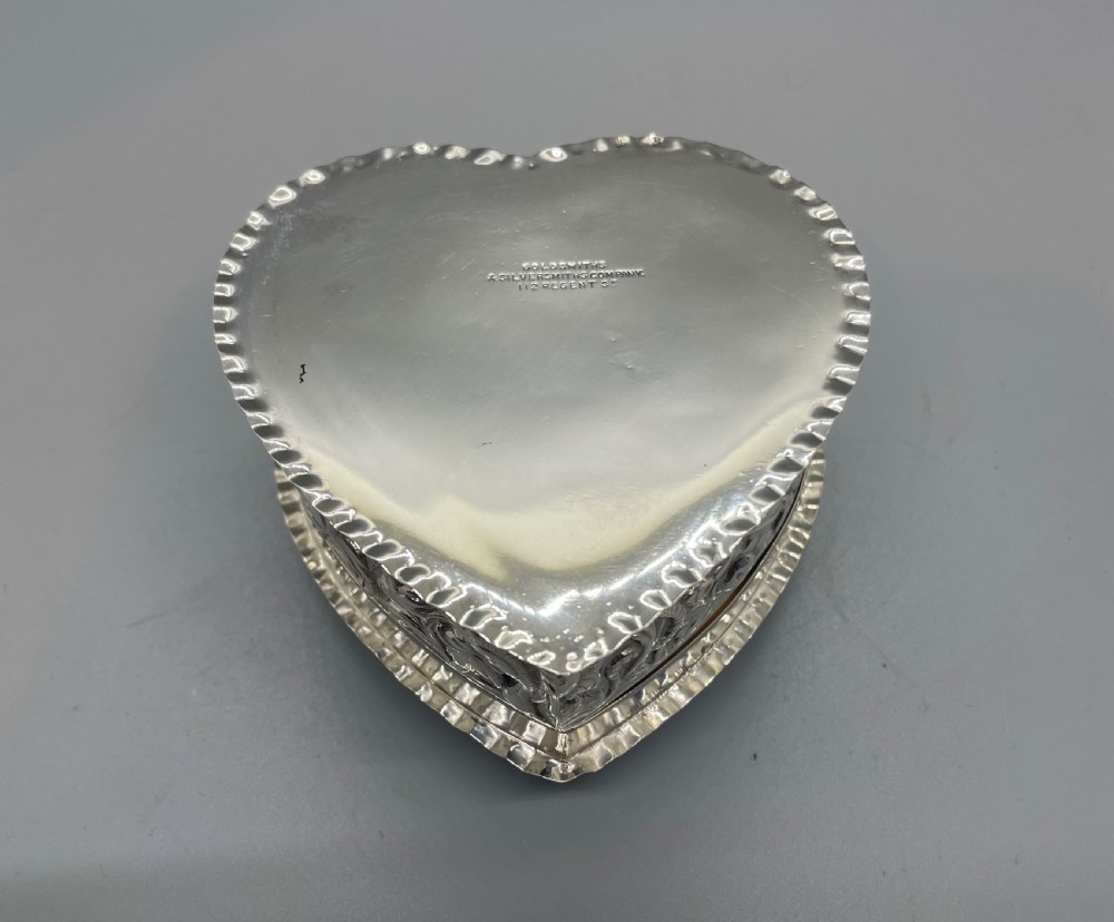 A heart-shaped sterling silver trinket box decorated with relief foliate scrollwork, a crimped rim, and a smooth central cartouche. View VII
