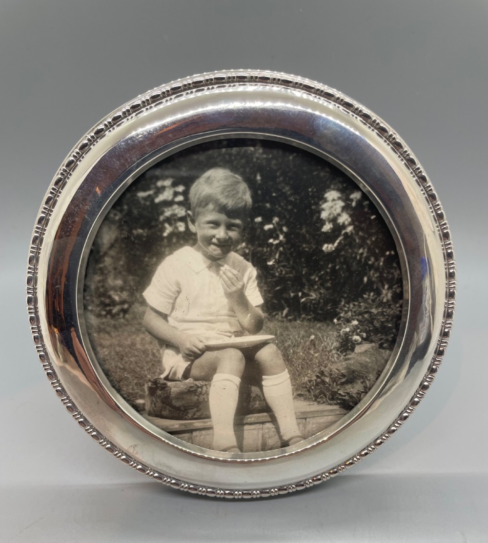 A circular George V sterling silver picture frame featuring a beaded outer rim, displaying a black and white photograph of a young boy.