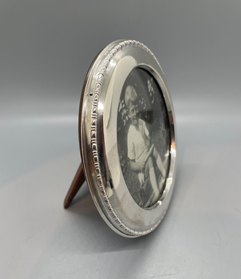 A circular George V sterling silver picture frame featuring a beaded outer rim, displaying a black and white photograph of a young boy. View II