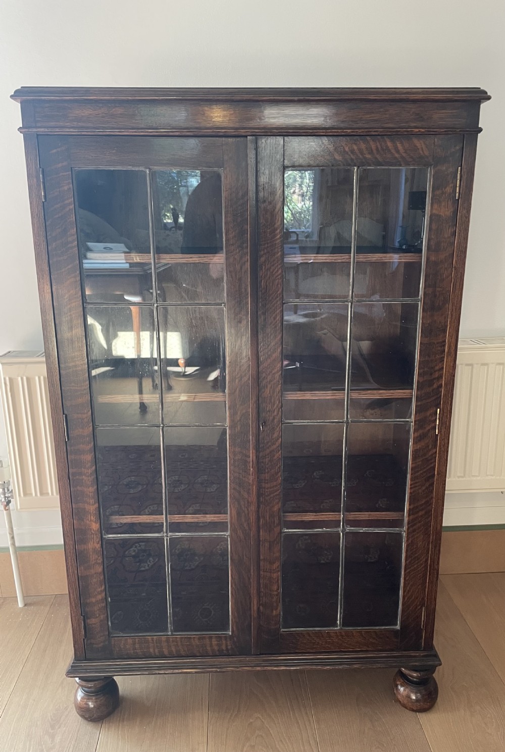 A 1920s dark oak bookcase featuring twin glazed doors with leaded glass panes, set on turned bun feet.