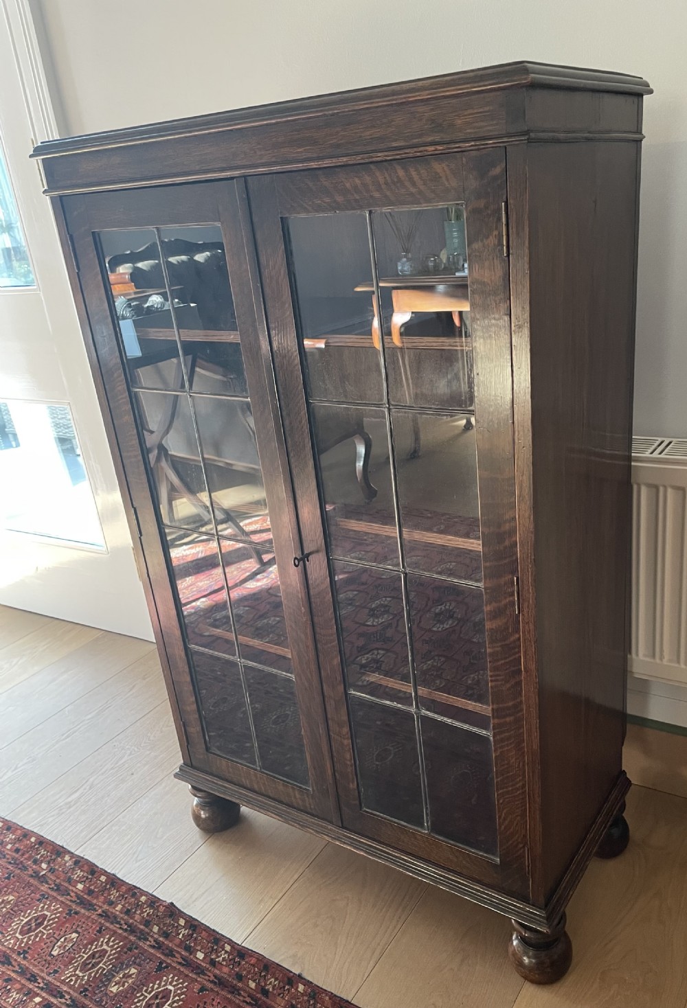 A 1920s dark oak bookcase featuring twin glazed doors with leaded glass panes, set on turned bun feet. View III