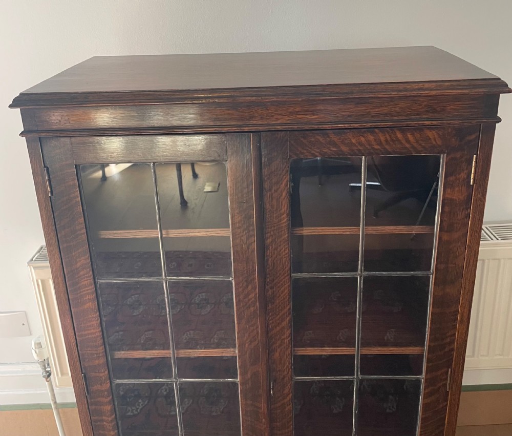 A 1920s dark oak bookcase featuring twin glazed doors with leaded glass panes, set on turned bun feet. View IV
