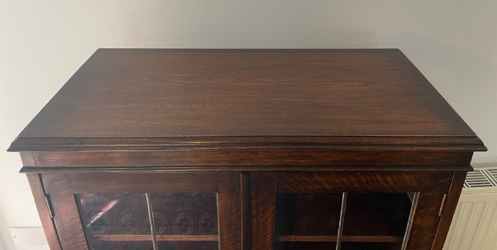 A 1920s dark oak bookcase featuring twin glazed doors with leaded glass panes, set on turned bun feet. View V