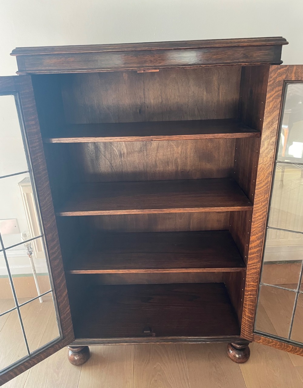 A 1920s dark oak bookcase featuring twin glazed doors with leaded glass panes, set on turned bun feet. View VI