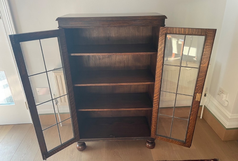A 1920s dark oak bookcase featuring twin glazed doors with leaded glass panes, set on turned bun feet. View VIII