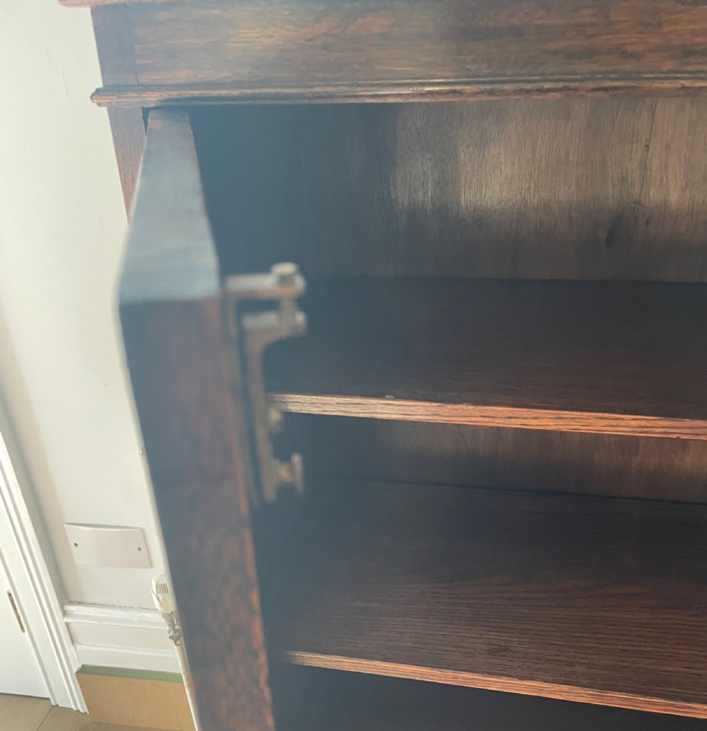 A 1920s dark oak bookcase featuring twin glazed doors with leaded glass panes, set on turned bun feet. View XI