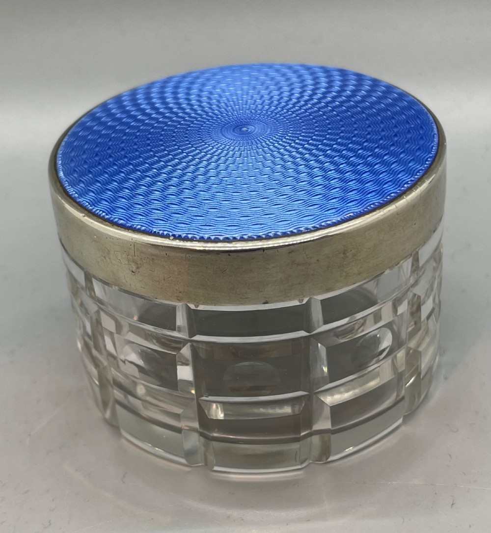 An Art Deco round clear glass vanity jar topped with a sterling silver rim and a blue engine-turned guilloche enamel lid. View II