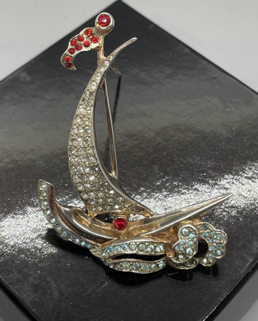A 1940s sterling silver gilt brooch in the shape of a sailing yacht set with clear, light blue, and red rhinestones.