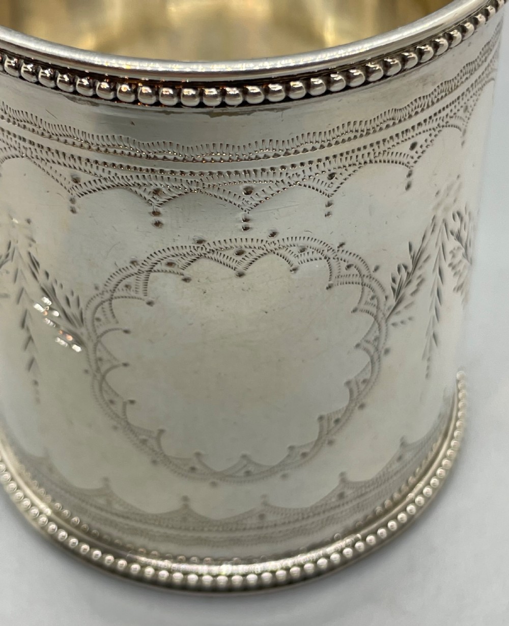 An antique sterling silver christening mug featuring floral engravings and beaded edges, placed beside its original fitted leather case lined with magenta velvet. View VII