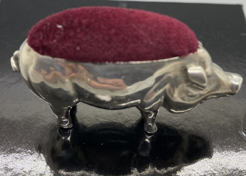 An Edwardian sterling silver pin cushion modelled in the shape of a standing pig with a red velvet pad on its back.