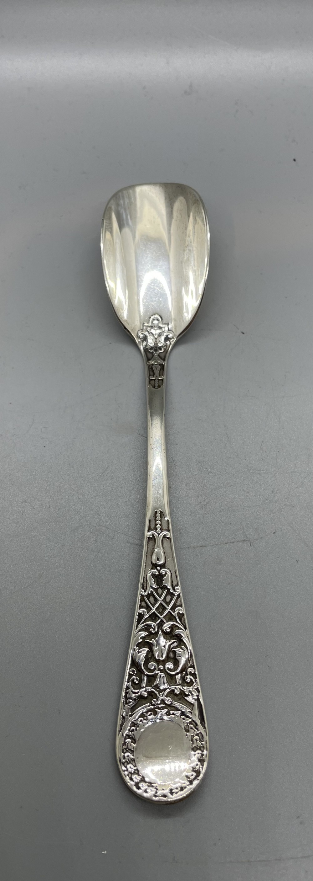 An Edwardian sterling silver stilton spoon displaying an ornate relief-carved handle with floral motifs and a polished scoop-shaped bowl.