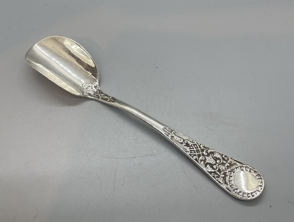 An Edwardian sterling silver stilton spoon displaying an ornate relief-carved handle with floral motifs and a polished scoop-shaped bowl. View II