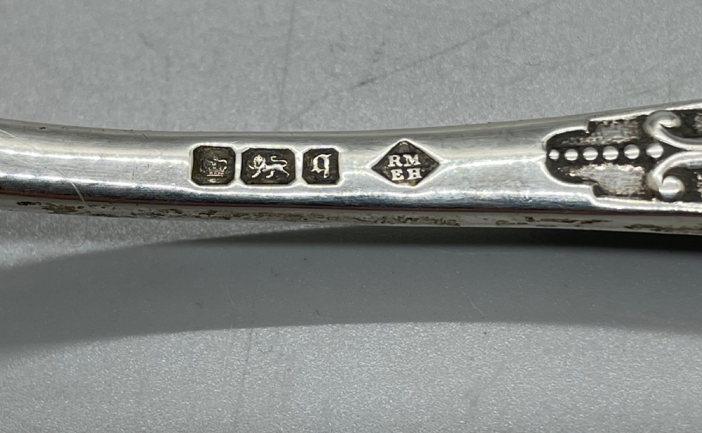 An Edwardian sterling silver stilton spoon displaying an ornate relief-carved handle with floral motifs and a polished scoop-shaped bowl. View IV