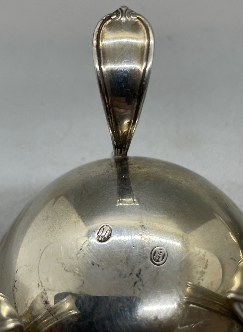 A Danish Art Deco silver tea strainer with a pierced bowl design and a smooth flat handle resting on a tripod stand. View III