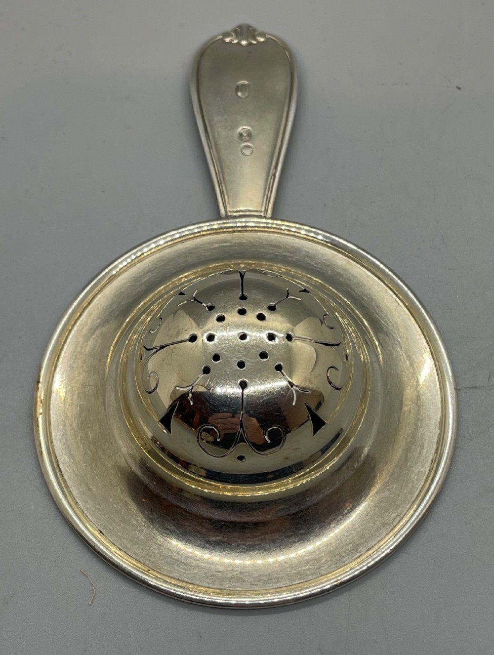 A Danish Art Deco silver tea strainer with a pierced bowl design and a smooth flat handle resting on a tripod stand. View VIII
