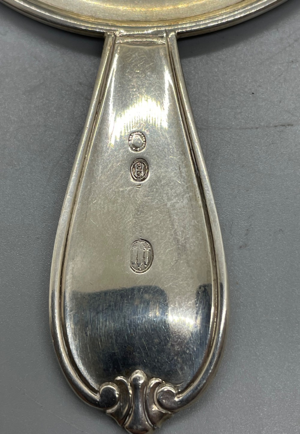 A Danish Art Deco silver tea strainer with a pierced bowl design and a smooth flat handle resting on a tripod stand. View IX