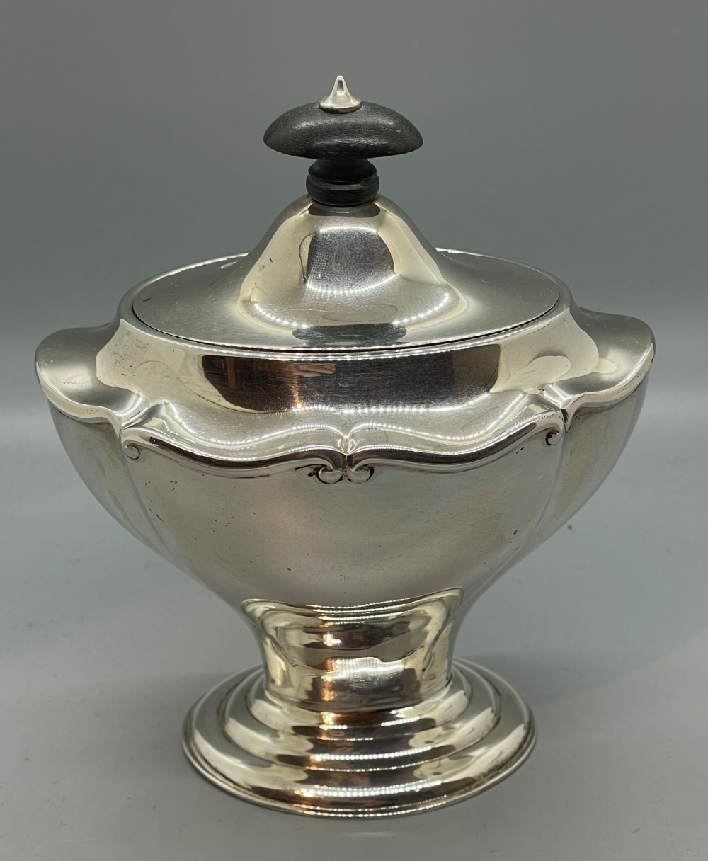 A George V sterling silver tea caddy with a lobed pedestal body, fitted lid, and a dark wooden finial.