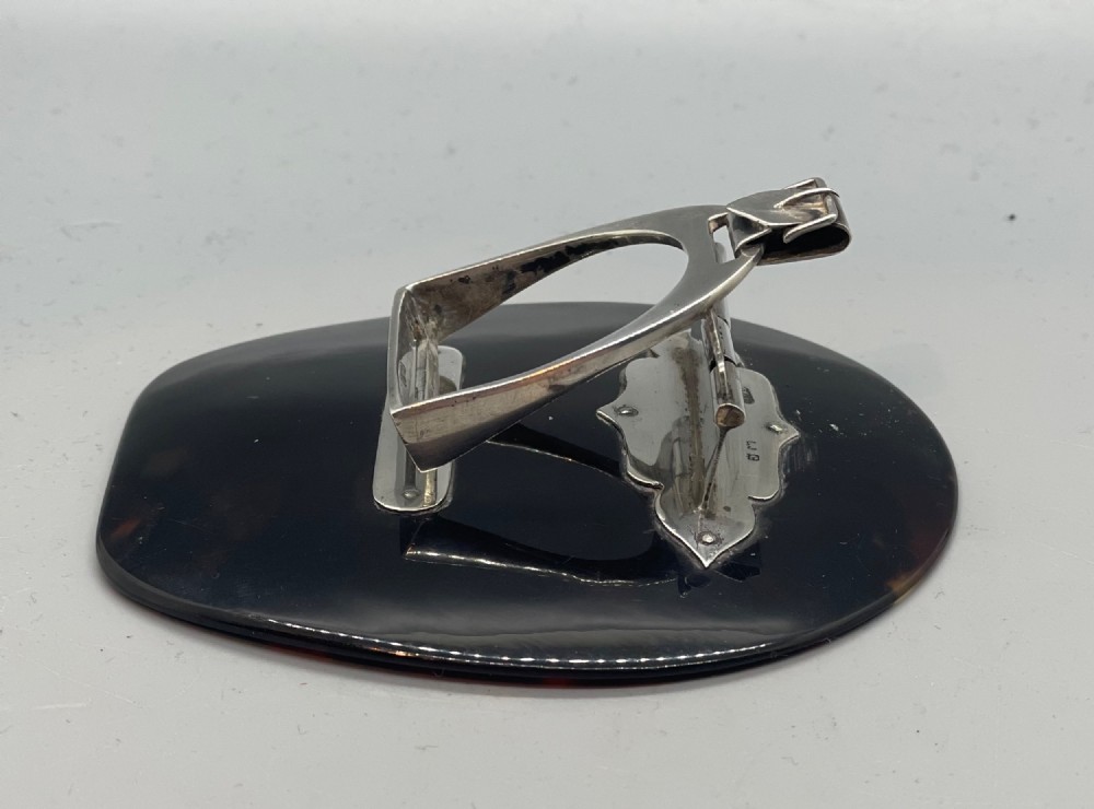 An Edwardian sterling silver letter clip styled as an equestrian stirrup on a smooth dark tortoiseshell base. View V
