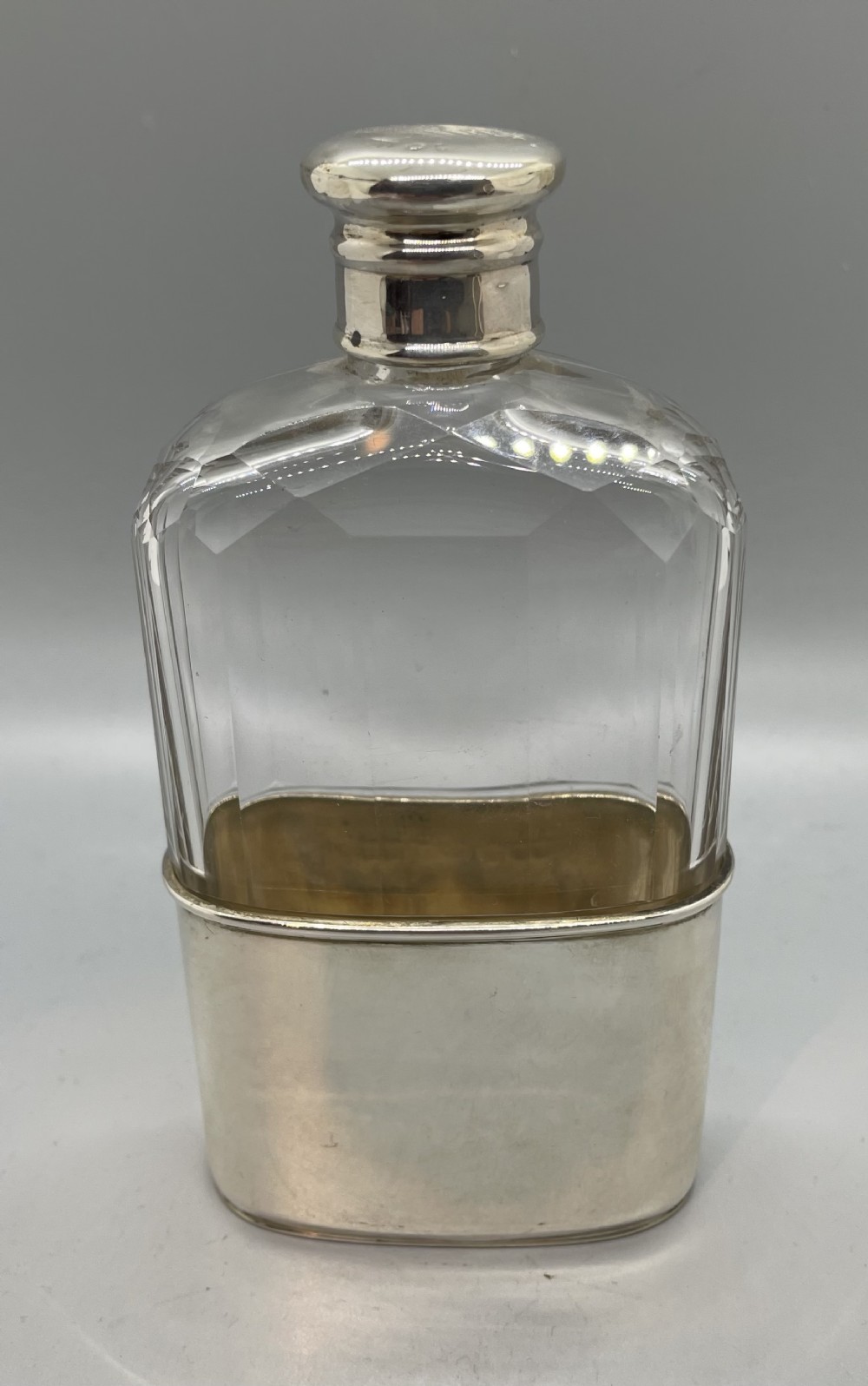 A Victorian glass spirit flask featuring a faceted clear glass upper section, a silver collar with cap, and a detachable silver base cup.