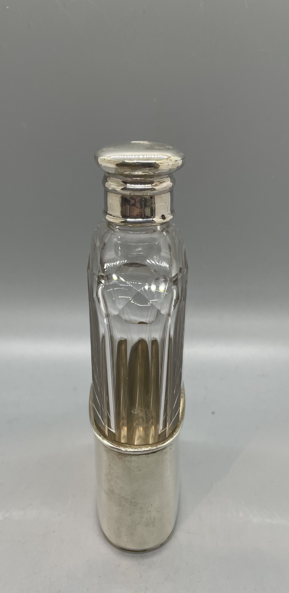 A Victorian glass spirit flask featuring a faceted clear glass upper section, a silver collar with cap, and a detachable silver base cup. View II