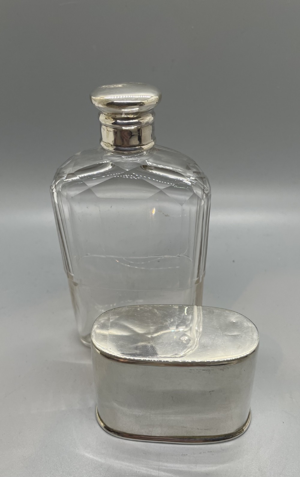 A Victorian glass spirit flask featuring a faceted clear glass upper section, a silver collar with cap, and a detachable silver base cup. View V