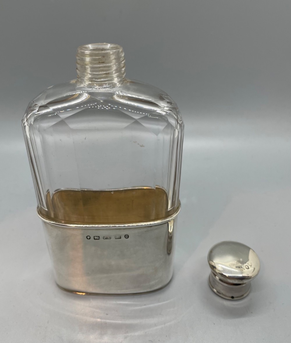 A Victorian glass spirit flask featuring a faceted clear glass upper section, a silver collar with cap, and a detachable silver base cup. View VI
