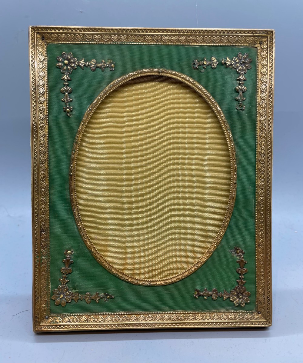An Edwardian rectangular metal photo frame with a green fabric mount, gilt floral corner appliques, and an oval aperture.