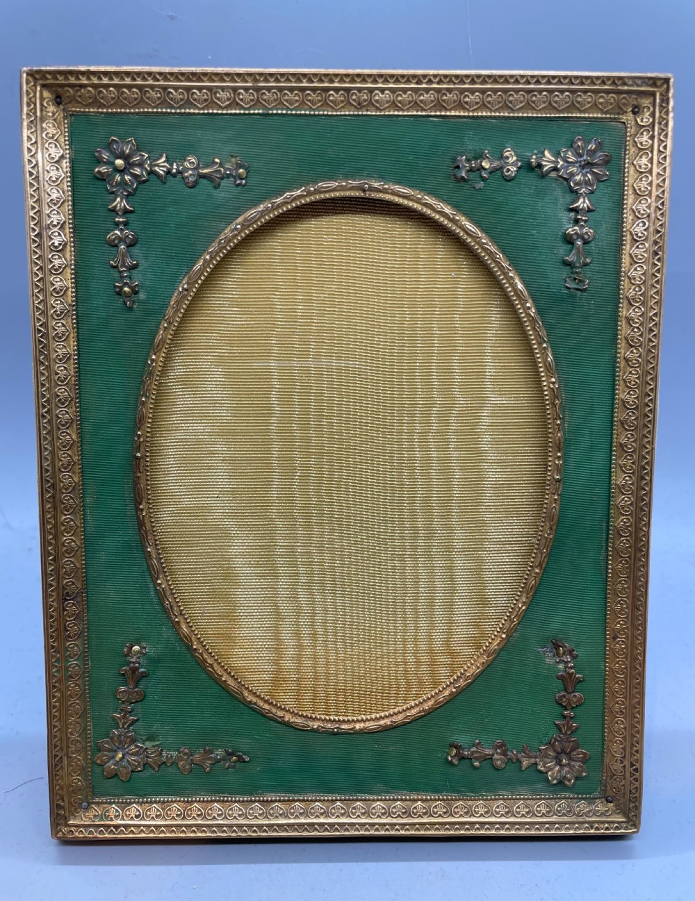 An Edwardian rectangular metal photo frame with a green fabric mount, gilt floral corner appliques, and an oval aperture. View II