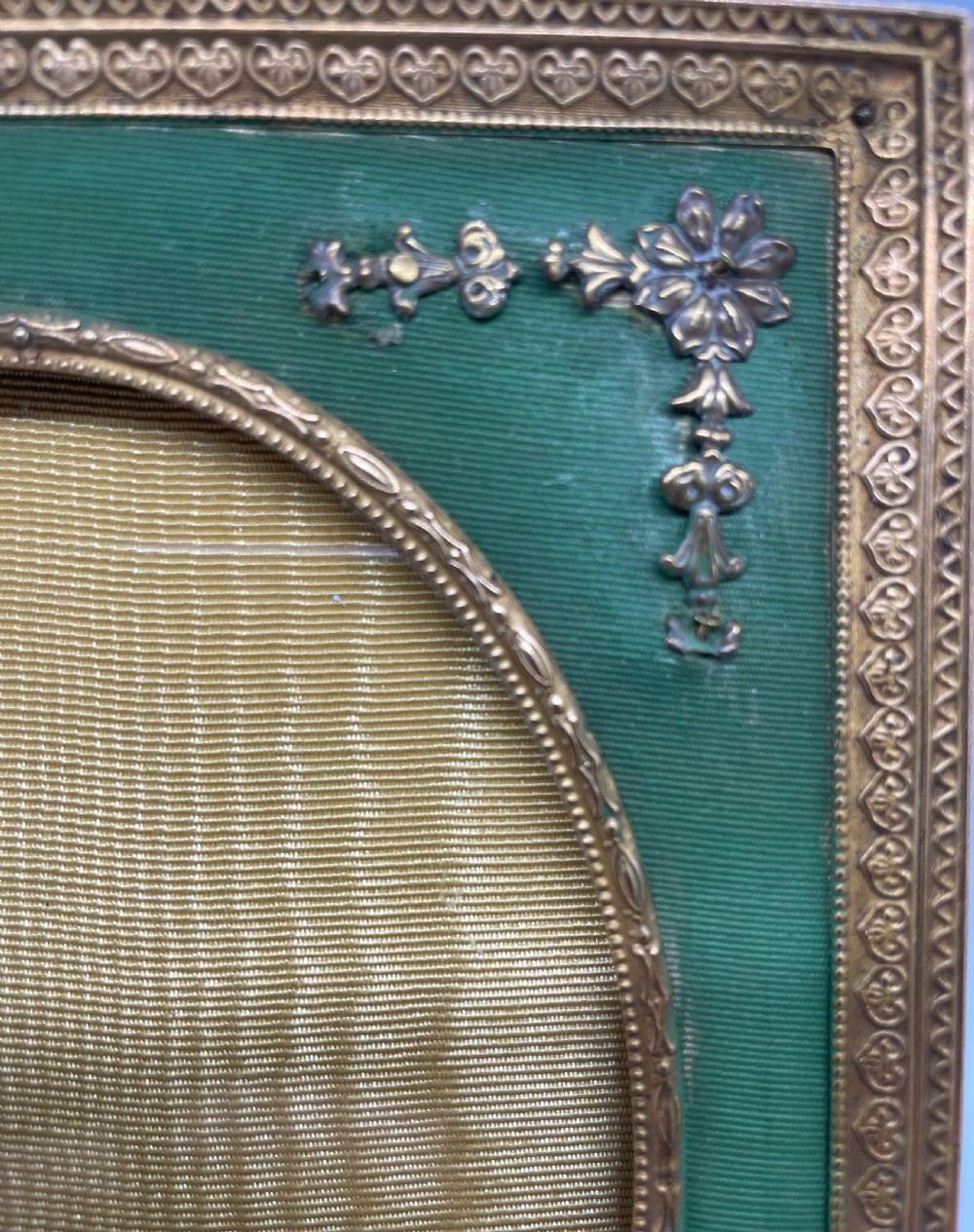 An Edwardian rectangular metal photo frame with a green fabric mount, gilt floral corner appliques, and an oval aperture. View IV