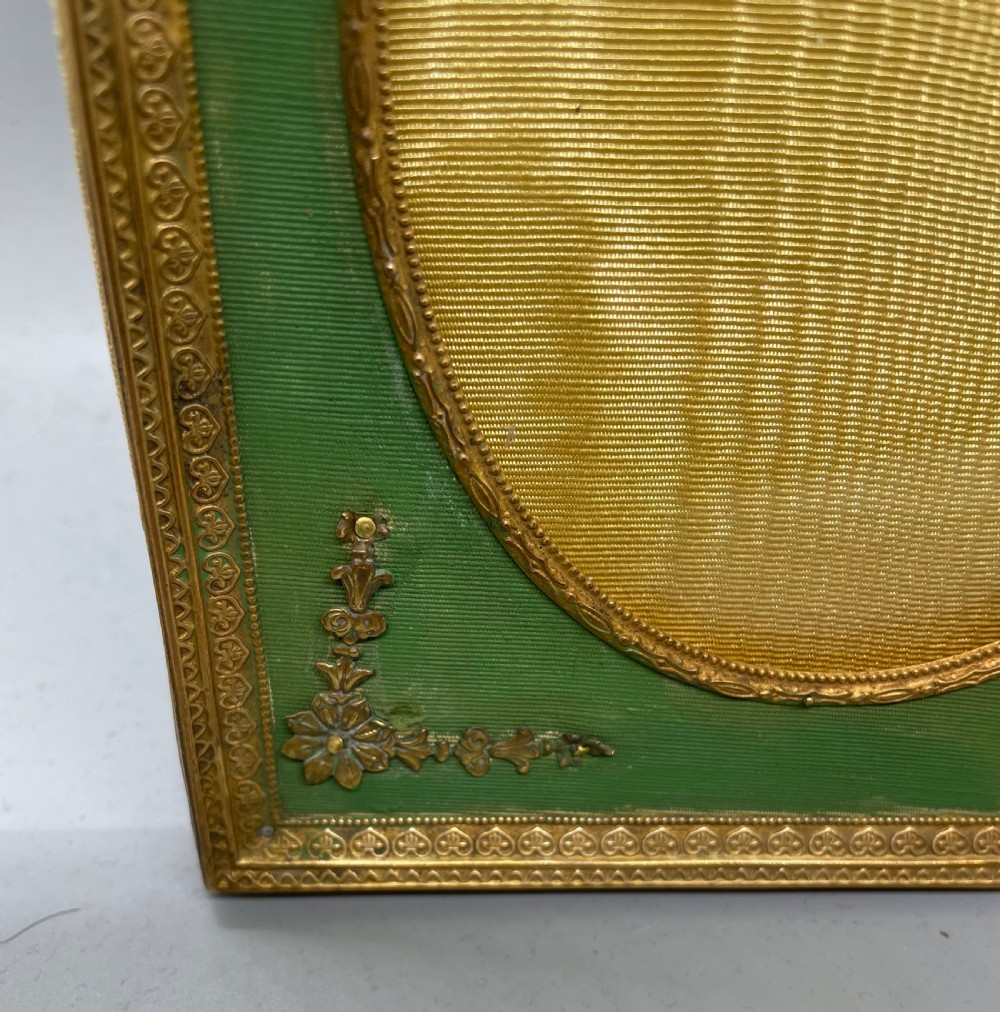 An Edwardian rectangular metal photo frame with a green fabric mount, gilt floral corner appliques, and an oval aperture. View V