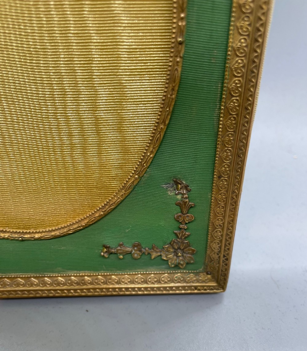 An Edwardian rectangular metal photo frame with a green fabric mount, gilt floral corner appliques, and an oval aperture. View VI
