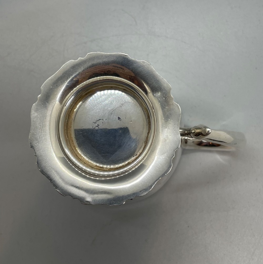 A polished sterling silver George V mug featuring a plain tapered body, an angular loop handle, and a scalloped pedestal base. View IX