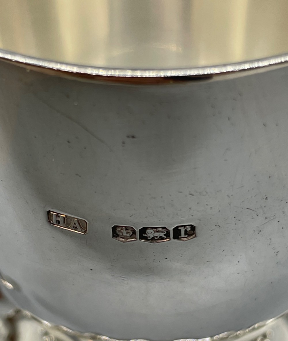 A polished sterling silver George V mug featuring a plain tapered body, an angular loop handle, and a scalloped pedestal base. View X