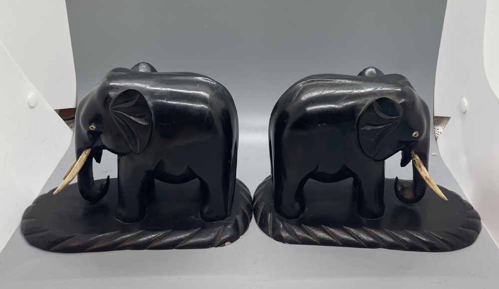 A pair of hand-carved dark wood elephant bookends from the Art Deco period, featuring light-coloured inlaid tusks and carved rope-twist edges on the bases.