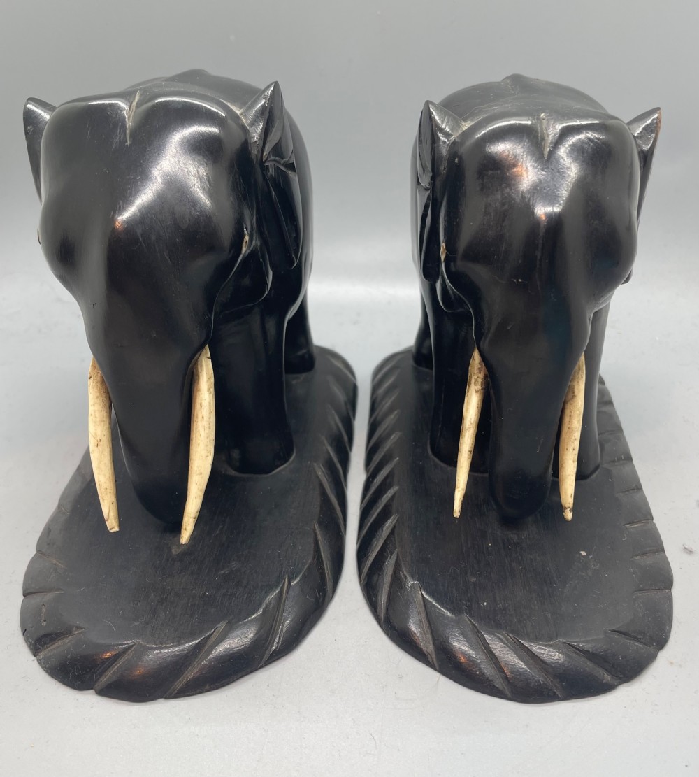 A pair of hand-carved dark wood elephant bookends from the Art Deco period, featuring light-coloured inlaid tusks and carved rope-twist edges on the bases. View V