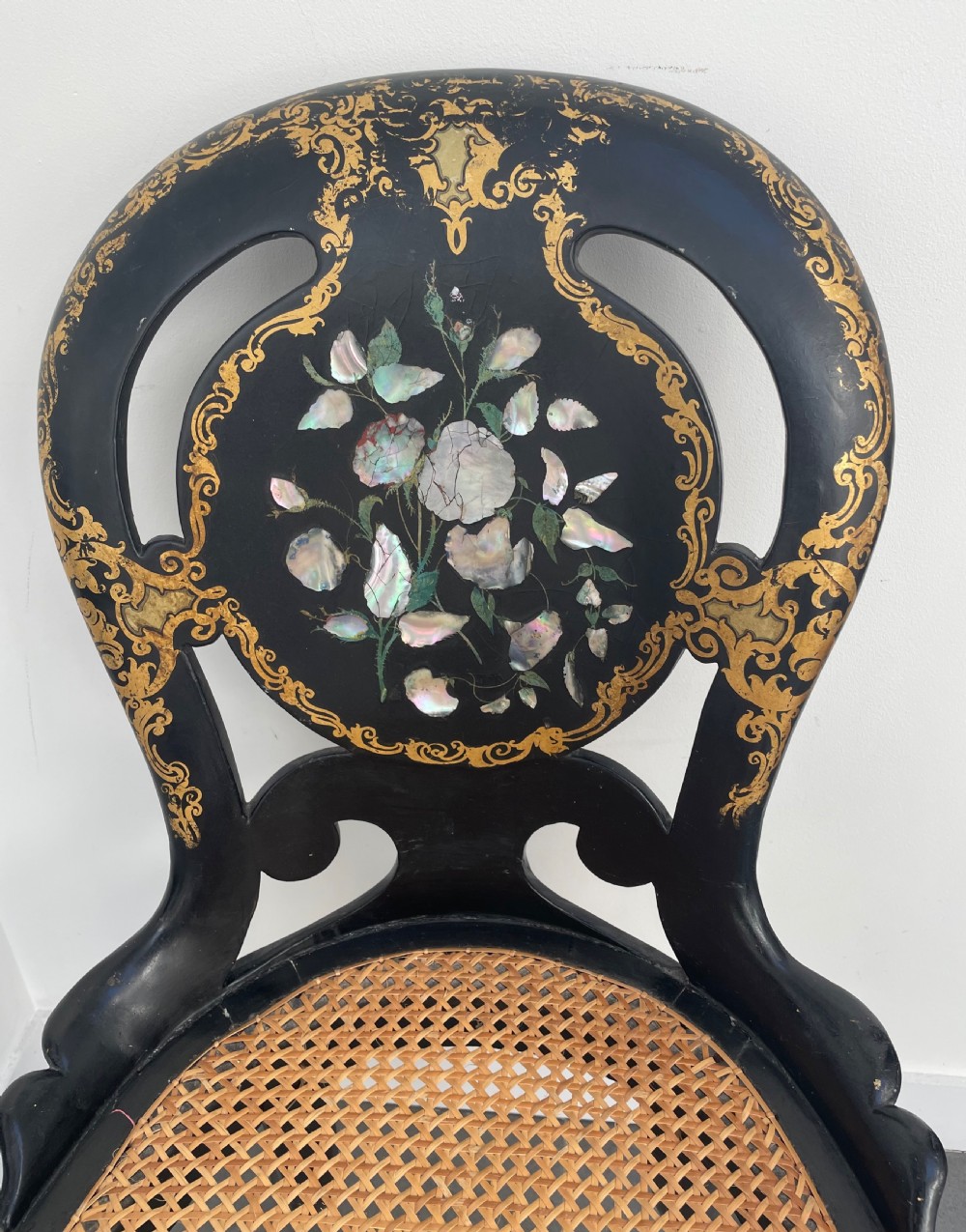 A Victorian ebonised side chair featuring floral mother-of-pearl inlays, gold leaf scrollwork decoration, a shaped back rest, cabriole front legs, and a woven cane seat. View II