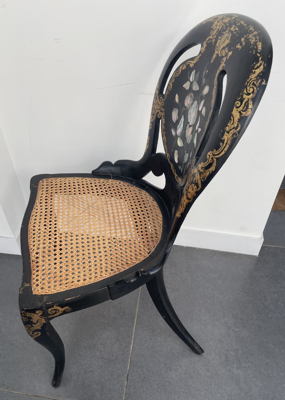 A Victorian ebonised side chair featuring floral mother-of-pearl inlays, gold leaf scrollwork decoration, a shaped back rest, cabriole front legs, and a woven cane seat. View VIII