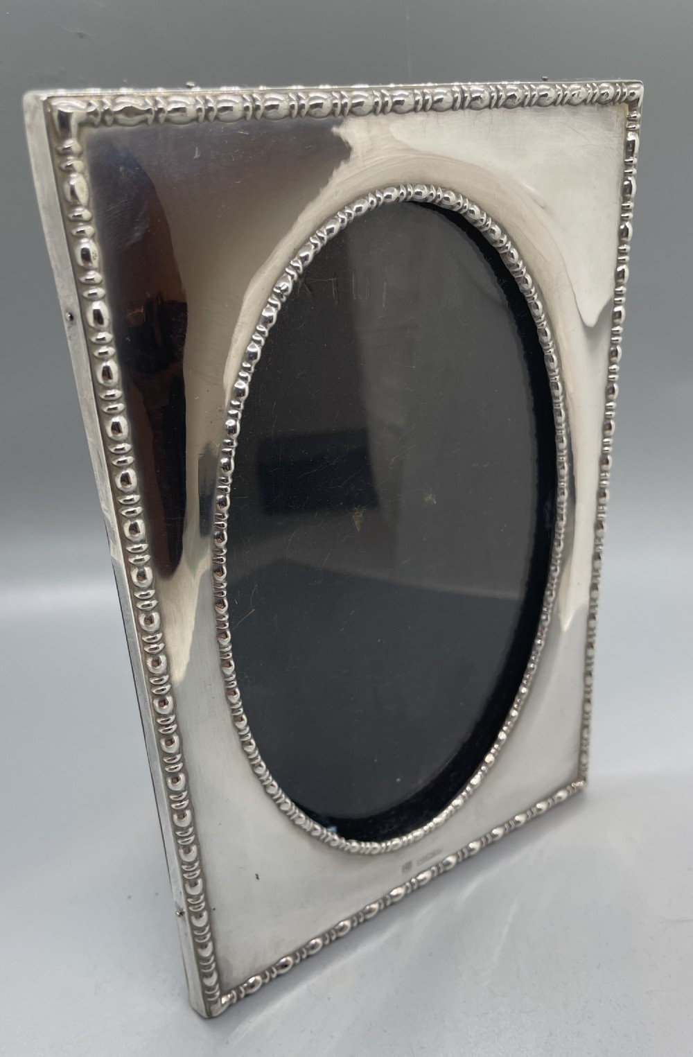 A rectangular sterling silver photo frame featuring an oval central aperture and a beaded rim detail. View VIII